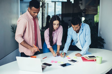 Male and female colleagues collaborating on information making notes during brainsorming at office desktop with laptop, diverse entrepreneurs concentrated during working process and briefing