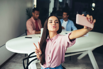 Positive female showing v-sign for taking funny pictures using application for blogging on...