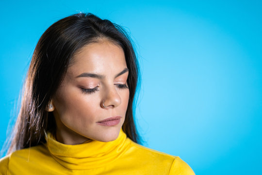 Beautiful cheerful mixed race woman in yellow clothing smiling over blue wall background. Cute hispanic girl's portrait.