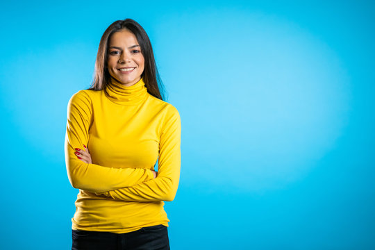 Copy space. Beautiful cheerful mixed race woman in yellow clothing smiling to camera over blue wall background. Cute hispanic girl's portrait.