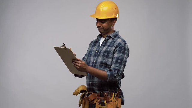 profession, construction and building - thinking indian worker or builder in helmet with clipboard and pencil over grey background