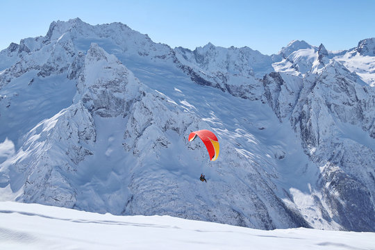 paraplane flying over snowy Caucasus mountains sunny blue sky