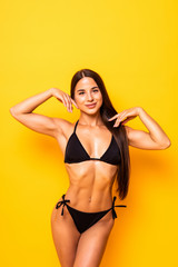 Young sexy slim tanned woman in black swimsuit posing against yellow background.