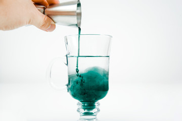 Pouring mint syrup into a glass of water. Beautiful green water color. Pouring the green dye into the water. The concept of preparing drinks.