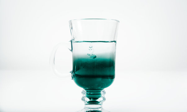 Pouring mint syrup into a glass of water. Beautiful green water color. Pouring the green dye into the water. The concept of preparing drinks.