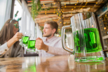 The company of young people celebrate St. Patrick's Day. They have fun at the bar. They are dressed...
