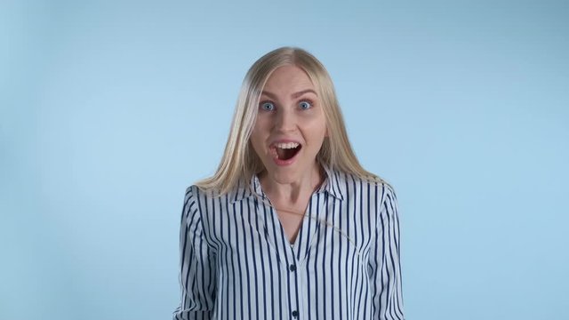 Blonde female widely opening her mouth in astonishment. Blue background.
