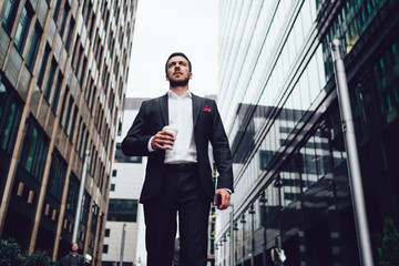 Below view of intelligent male entrepreneur dressed in luxury suit walking near skyscrapers in...