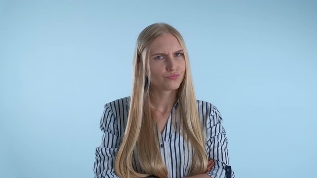 Offended blonde woman refusing to do something on blue background. She is angry and sad.