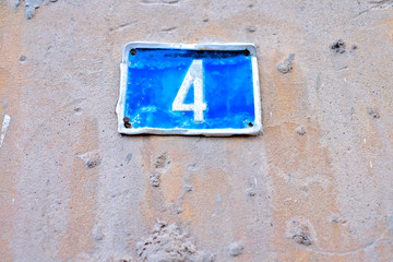 Number 4, four, blue plate on a pale weathered wall.