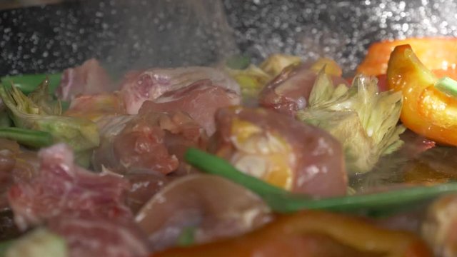 slow motion meat cooking on an open fire with vegetables for a paella