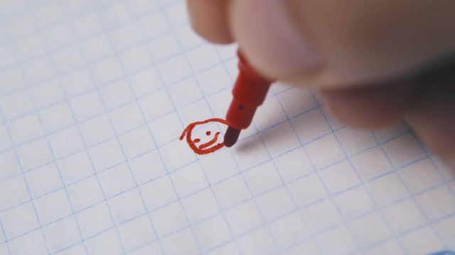 young man draws funny human figure using red marker on checkered paper sheet extreme close view