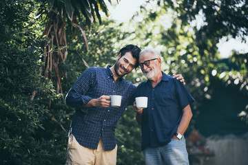 An adult hipster son and his senior father in garden, hugging