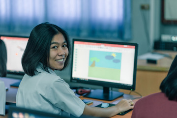 A smiling Asian female high school student in white uniform is learning in computer room.