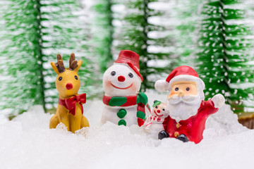 Happy Santa Claus and his reindeer with the snowman on snow with background of blurred Christmas pine.