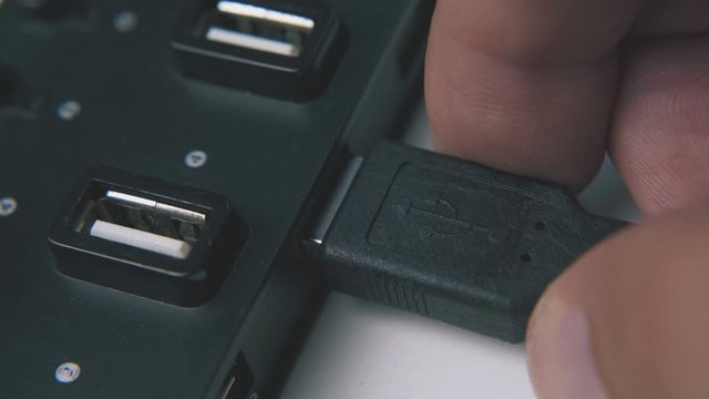 young man connects usb cable to modern hub in black plastic case on white background extreme close view
