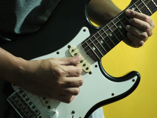 Asian man play electric guitar with yellow backdrop