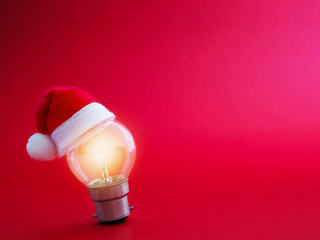 Light bulb and Santa Claus hat over red background with copy space.