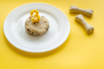 Birthday treat for puppy concept. Dog feed, candle in shape of number three, bones on yellow background copy space