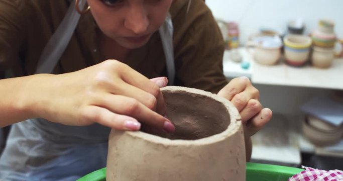 Female ceramist making raw clay earthenware pot vase in handcraft classroom with teacher support. Arts studying process. Handmade freelance creativity. Art university degree. Ceramic bowls manufacture