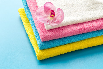 Obraz na płótnie Canvas Clean towels - stack of laundred linen with orchid flower - on blue background copy space