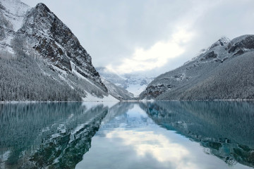 Lake Louise in early winter with first snow and storm clouds reflecting in calm turquoise  water. Canadian Rockies. Banff National Park. Alberta. Canada