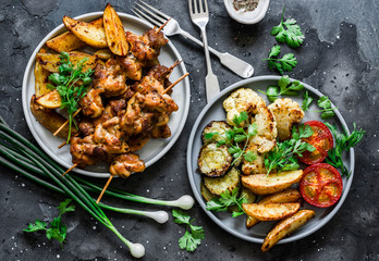 Meat skewers kebab with baked potatoes and roasted zucchini, tomatoes, cauliflower on a dark background, top view. Delicious tapas, appetizers in mediterranean style