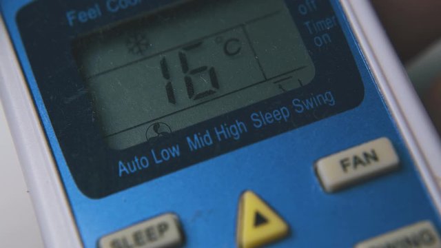 person lowers temperature pressing buttons on air conditioner remote control extreme close view