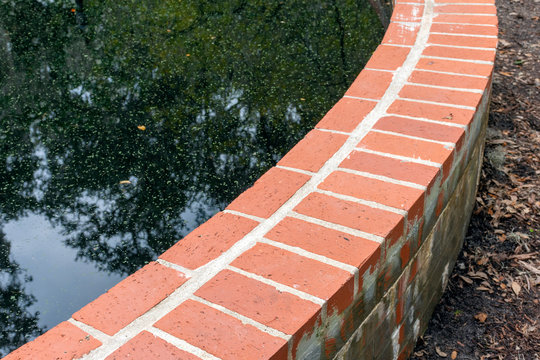 Close Up Detail Of A Curved Brick Retaining Wall Which Contains A Raised Pond.