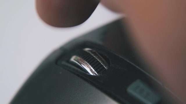 person turns wheel on contemporary black computer mouse in white background extreme close view