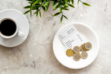 Pay restaurant bill by cash. Reciept and coins on plate on grey background top view