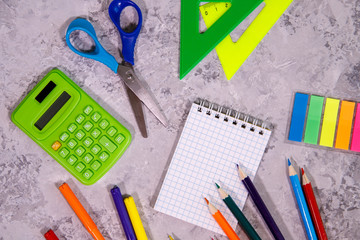 A set of stationery. Notepad, calculator, colored pencils, rulers, felt-tip pens, scissors and colorful stickers on a gray background. Space for text, background. Flat lay, top view