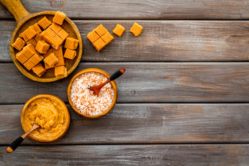 Prepare salted caramel. Scoop with sweet cubes, melted caramel and salt on dark wooden background top view copy space
