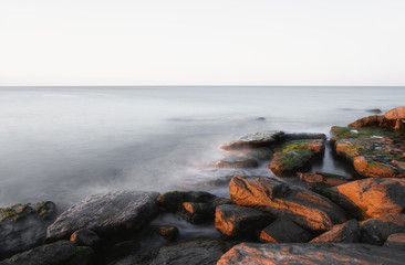 Fototapeta na wymiar Rocky sea shore with blurred calm water at sunrise