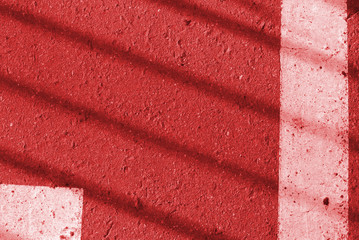 Asphalt surface with old white paint and fence shadow on it. Abstract background red color toned