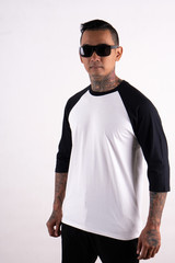 Young hipster man with tattoo wearing sunglasses standing while posing. Ready for your mock up template design or background. Young man wearing raglan 3/4 sleeve t shirt isolated on white background.