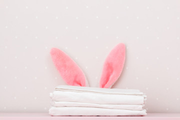 Close-up stack of clean white bedding and the Easter bunny ears, on the dressing table, on the background light walls. Copy space