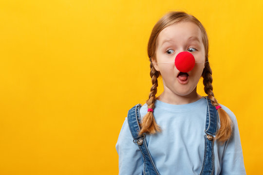 Funny child clown with a red nose. Cheerful little girl on a yellow background. April 1st Fool's Day. Copy space