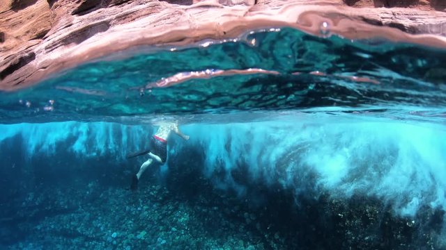 Man Snorkeling In Waves Beside A Cliff In Tropical Sea