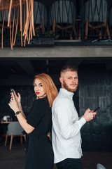 Young people stand with their backs to each other with a smartphones in hands.