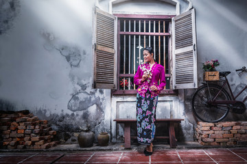 Beautiful Asian woman wearing Nyonya dress her hand holding plastic flower with old house, The dress of Paranakan woman in southeast Asia, Chinese Malay mix Traditional costume Asia, Ranong Thailand