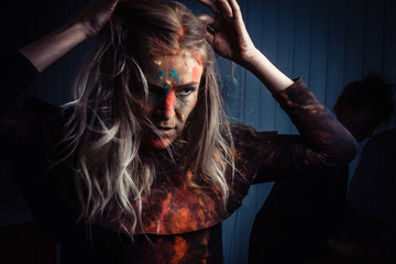 Beautiful young woman Holi paint fest with colorful powder covering her face and a cloud of dust. On black with rainbow bursts of color