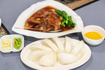 Steam pork leg with gravy and vegetable served soft white wheat bun or rice on table.