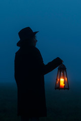 Woman is holding an iron lantern, with candle inside, in her hands