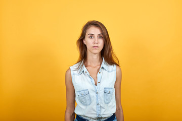 Obraz premium Disappointed caucasian young woman in blue denim shirt looking strict and serious isolated on orange background in studio. People sincere emotions, lifestyle concept.
