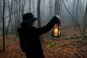 Young woman walks through the dark forest, she is holding an iron lantern © agneskantaruk