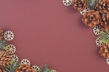 Seasonal Christmas flat lay with pine or fir cones and branches and wooden snowflake ornaments and white snowballs around edges of brown background with empty copy space in middle