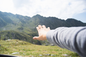 Hand of tourist straining after big green mountains