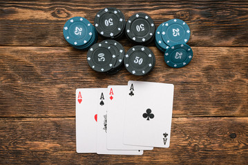 Poker chips and four aces cards on wooden table background.
