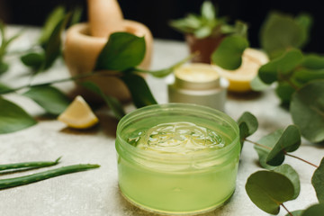 Creation of natural cosmetics from plants, natural . Face cream and aloe gel in jars on a gray orange background. Herbal dermatology cosmetic hygienic cream with flowers skincare product